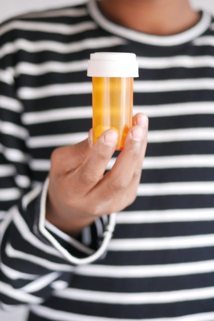 Close-up of a hand holding an empty prescription medicine bottle against a striped shirt backdrop.