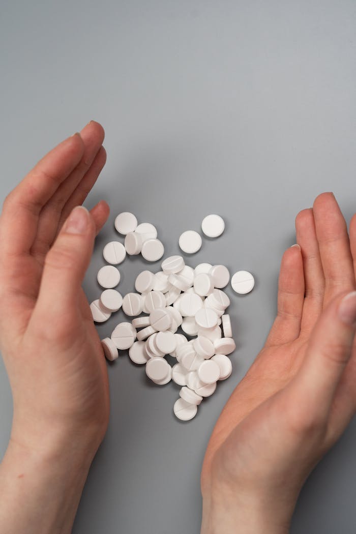 A close-up of hands near a pile of white tablets on a grey surface.