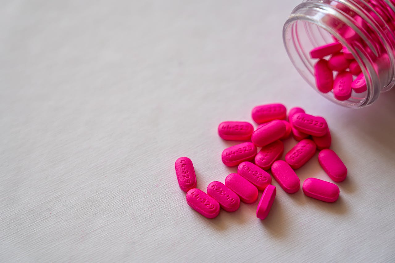 brand-01 Pink pills spilling from a glass bottle onto a surface, highlighting pharmaceutical care and medication.